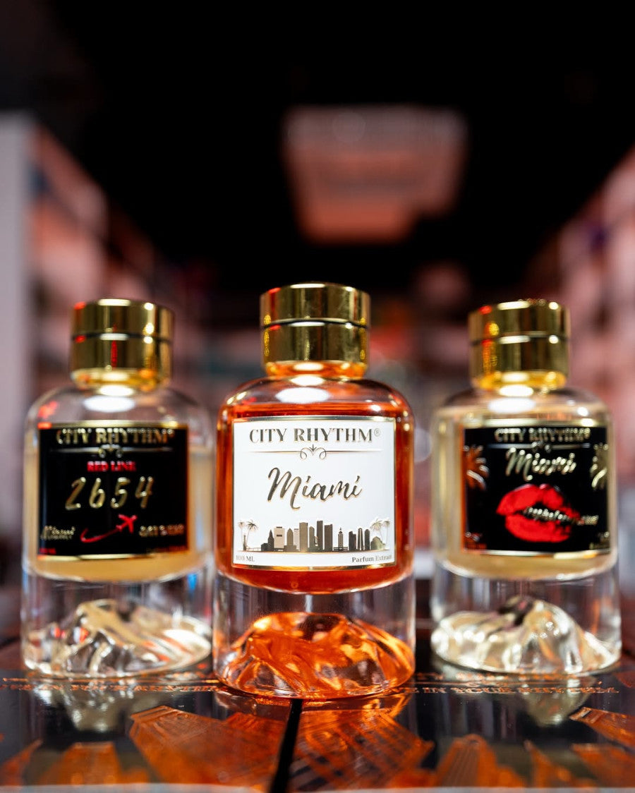 Image of three City Rhythm fragrances lined up side to side. From Left to right, City Rhythm's 2654 with a clear and gold bottle and black label with gold letters and hints of red on it, in the middle of the image is City Rhythm's Miami perfume bottle with a white label and gold and white perfume bottle, and finally to the right is a bottle of City Rhythm's Tropical Confessions Miami with a Gold and clear bottle plus a black, gold, and red label which has lipstick lips on it.