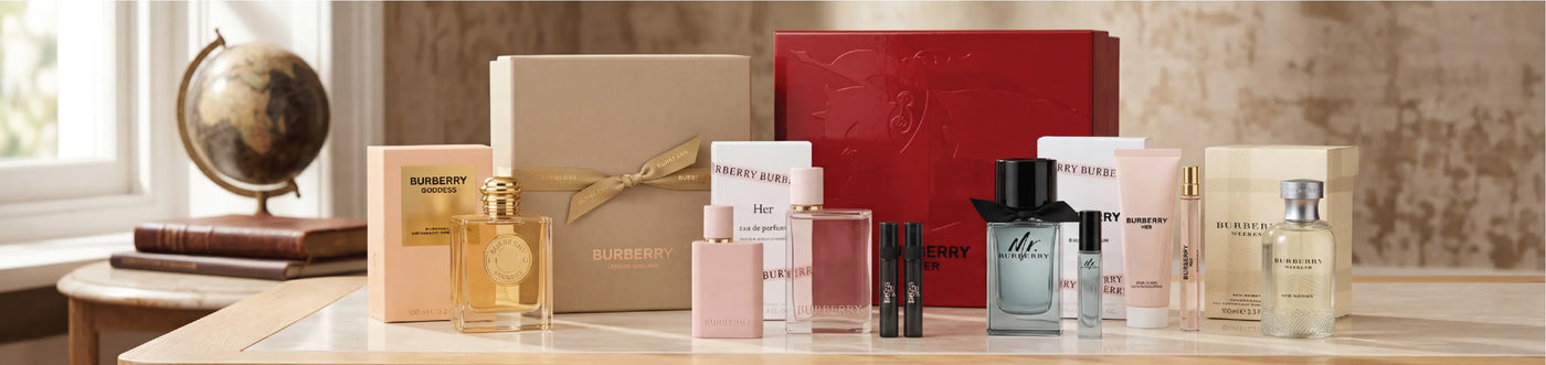 This is a banner image for the Burberry perfume brand. There are various perfume bottles neatly arranged accross a white marble table. The table is set next to a window in which the sun is shining through. The light beams are reflecting atop the table and glistening through the perufme bottles. From left to right, the perfume bottles read; Goddess, Her, Mr. Burberry, and Burberry Weekend.